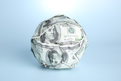 Photo of Ball made of dollars on light blue background