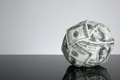 Photo of Ball made of dollars on black mirror surface. Space for text