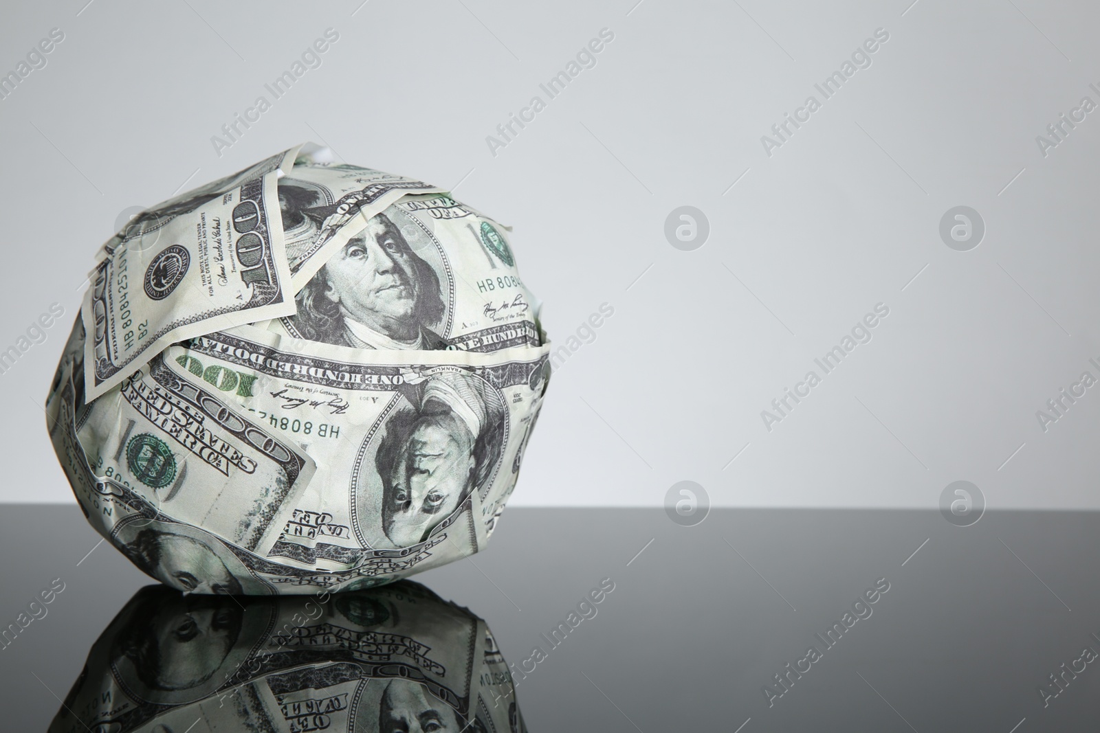 Photo of Ball made of dollars on black mirror surface. Space for text