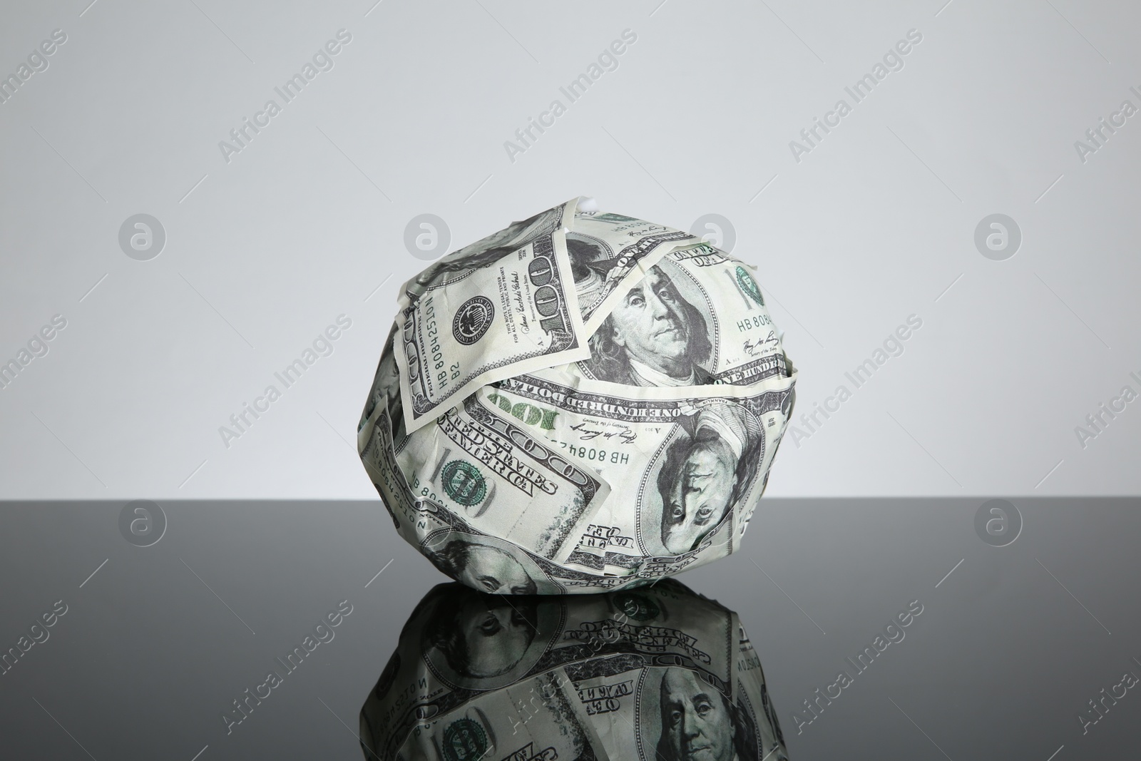 Photo of Ball made of dollars on black mirror surface