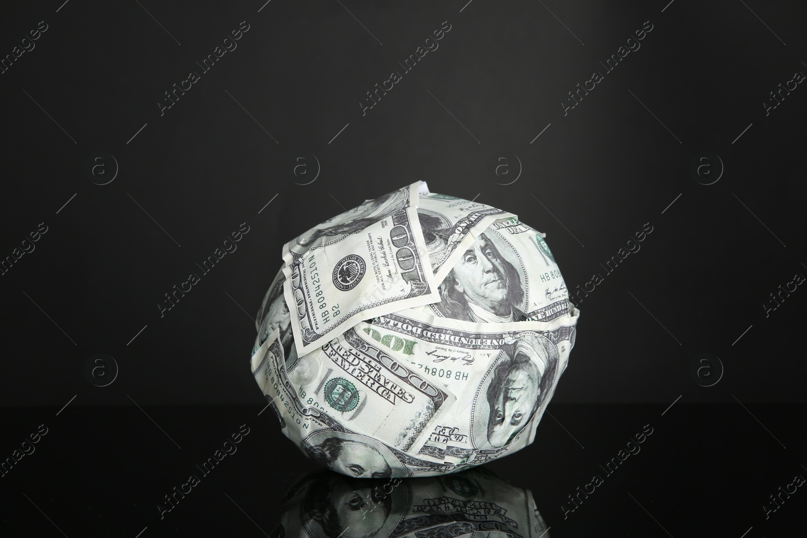 Photo of Ball made of dollars on black mirror surface