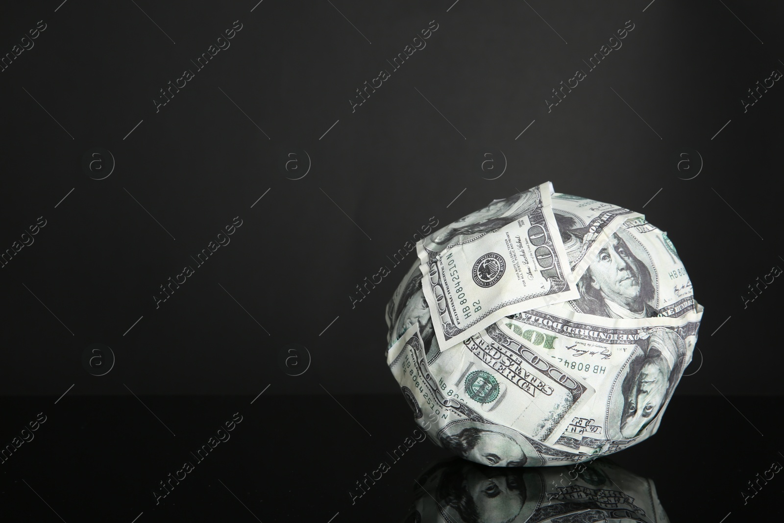 Photo of Ball made of dollars on black mirror surface. Space for text