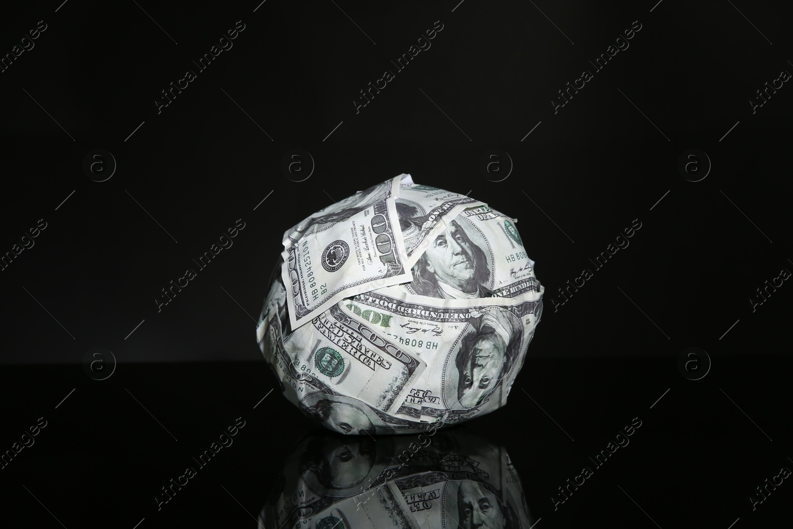 Photo of Ball made of dollars on black mirror surface