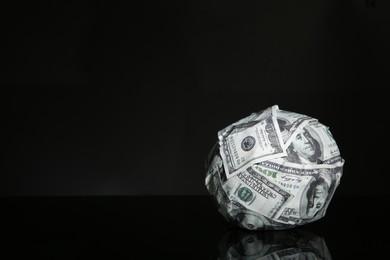 Photo of Ball made of dollars on black mirror surface. Space for text