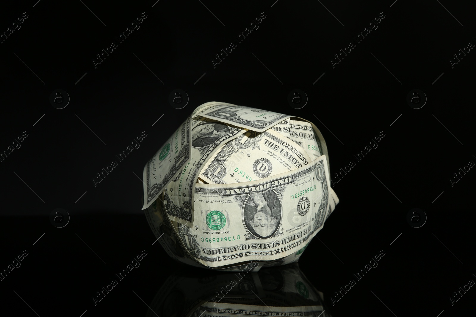 Photo of Ball made of dollars on black mirror surface