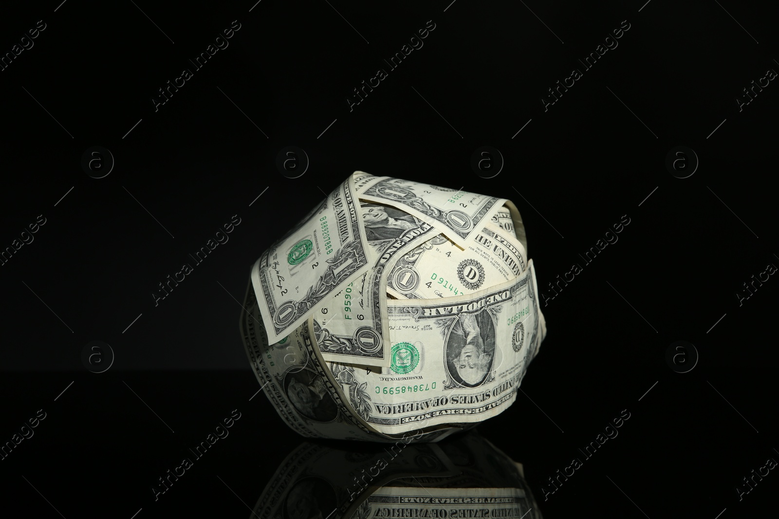 Photo of Ball made of dollars on black mirror surface