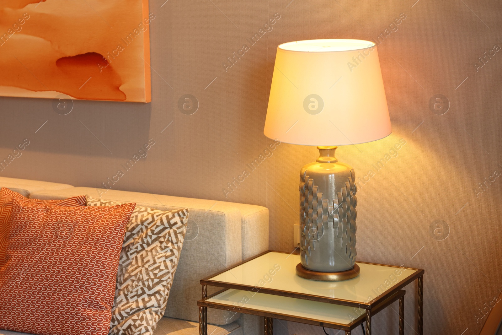 Photo of Comfortable sofa with cushions and lamp on side table in room