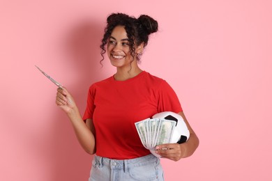 Happy woman with money and soccer ball on pink background