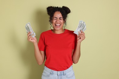 Happy woman with dollar banknotes on pale green background