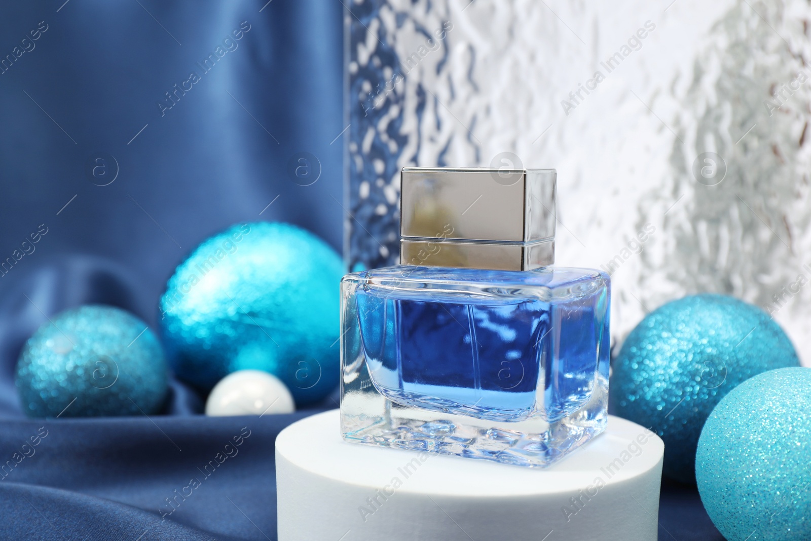 Photo of Stylish composition of perfume bottle and baubles on blue cloth