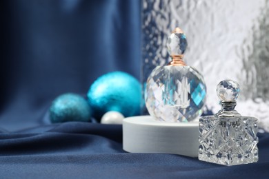 Stylish composition of perfume bottles and baubles on blue cloth. Space for text