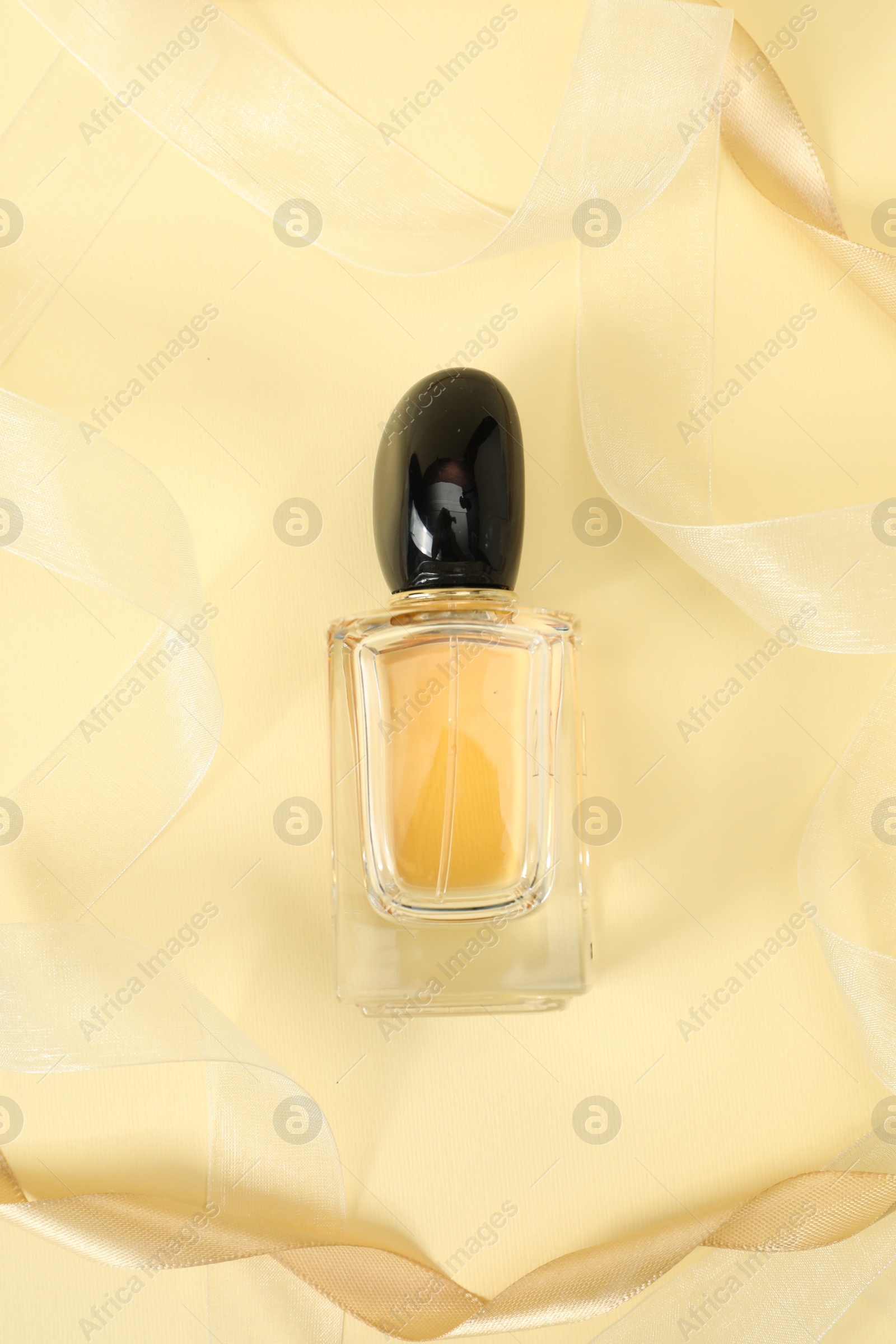 Photo of Stylish composition of perfume bottle and ribbons on beige background, top view