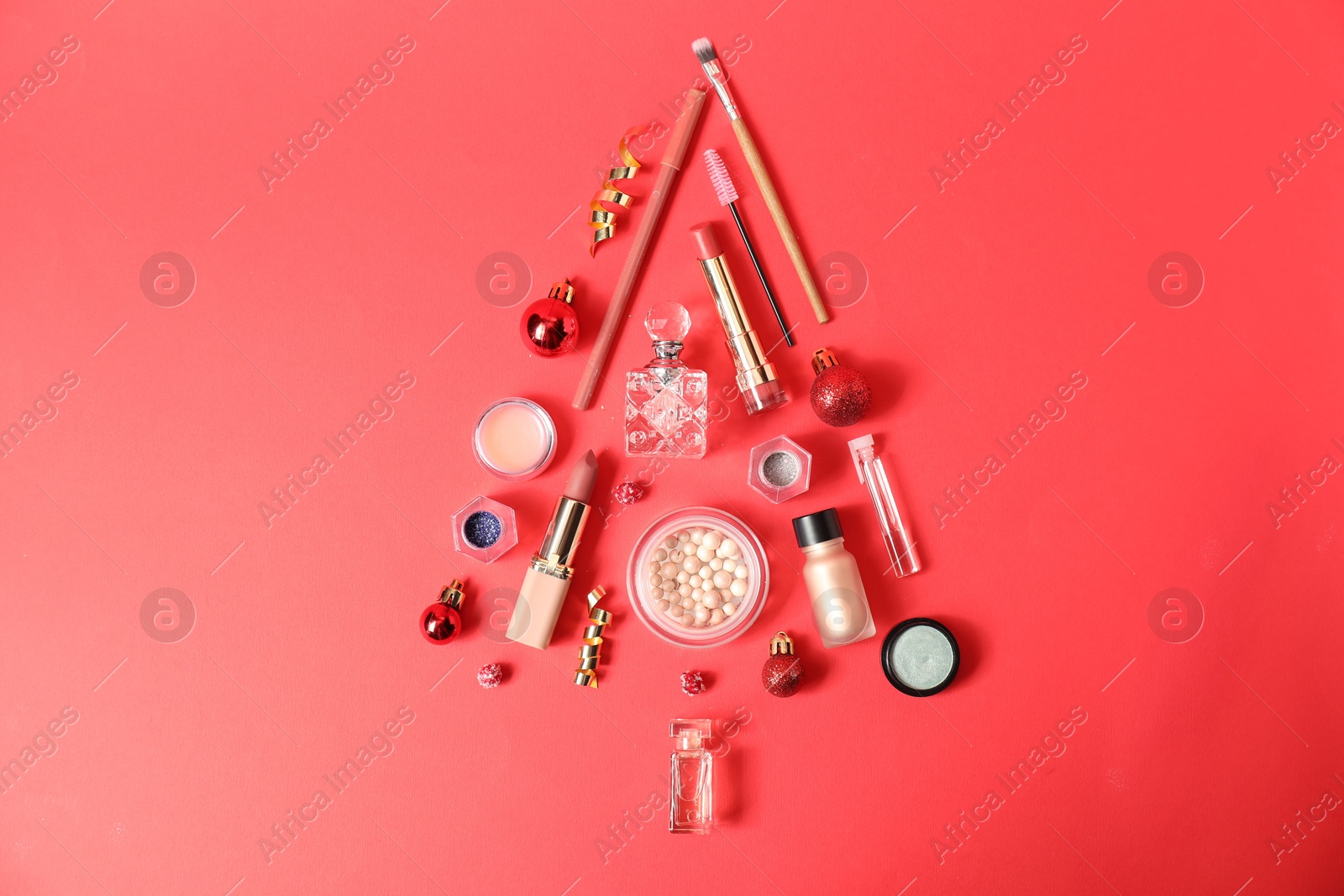 Photo of Christmas tree made of perfume bottles and makeup products on red background, flat lay