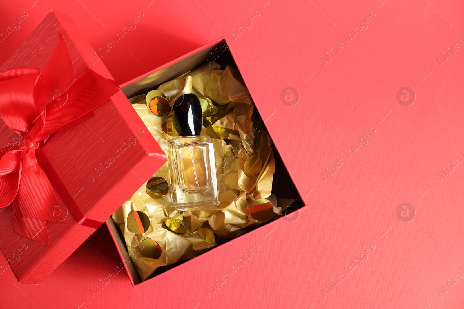 Photo of Open gift box with perfume bottle on red background, top view. Space for text