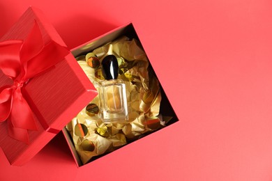 Open gift box with perfume bottle on red background, top view. Space for text