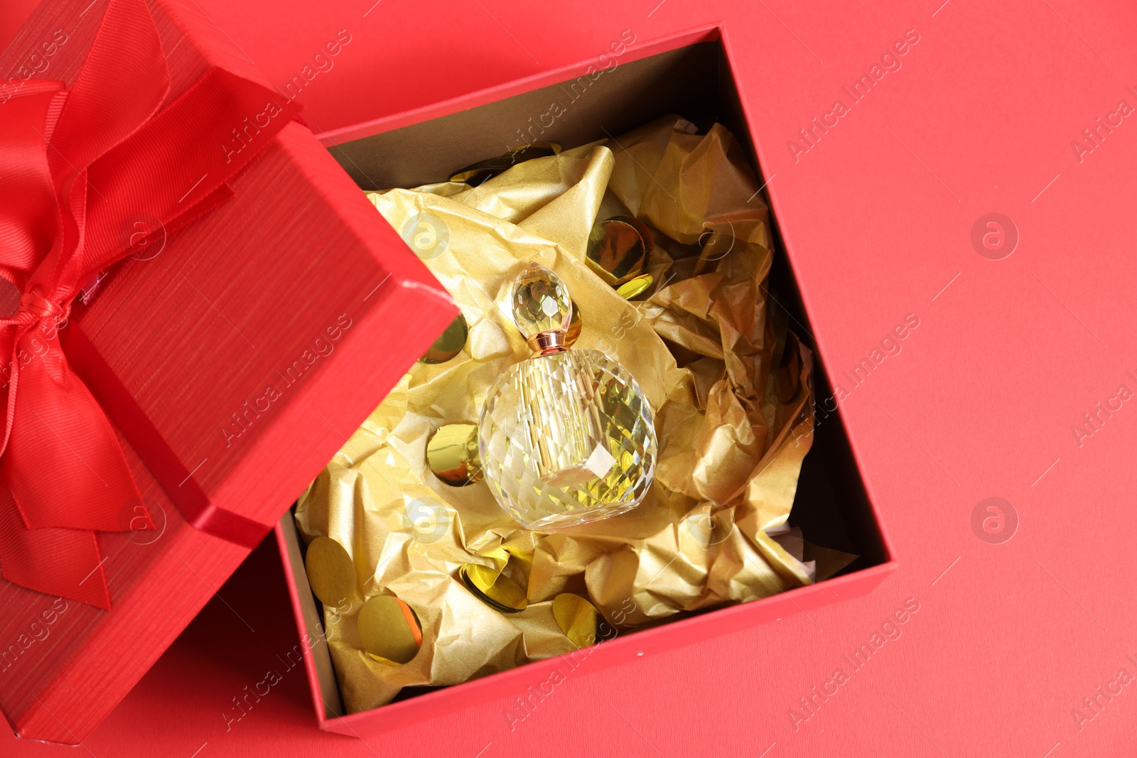 Photo of Open gift box with perfume bottle on red background, top view. Christmas present