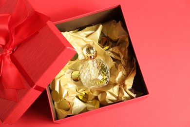 Photo of Open gift box with perfume bottle on red background, top view. Christmas present