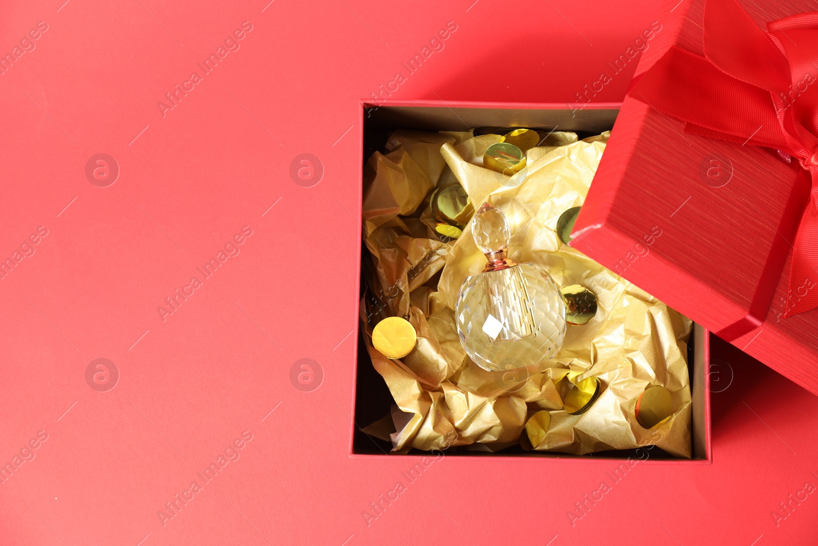 Photo of Open gift box with perfume bottle on red background, top view. Space for text