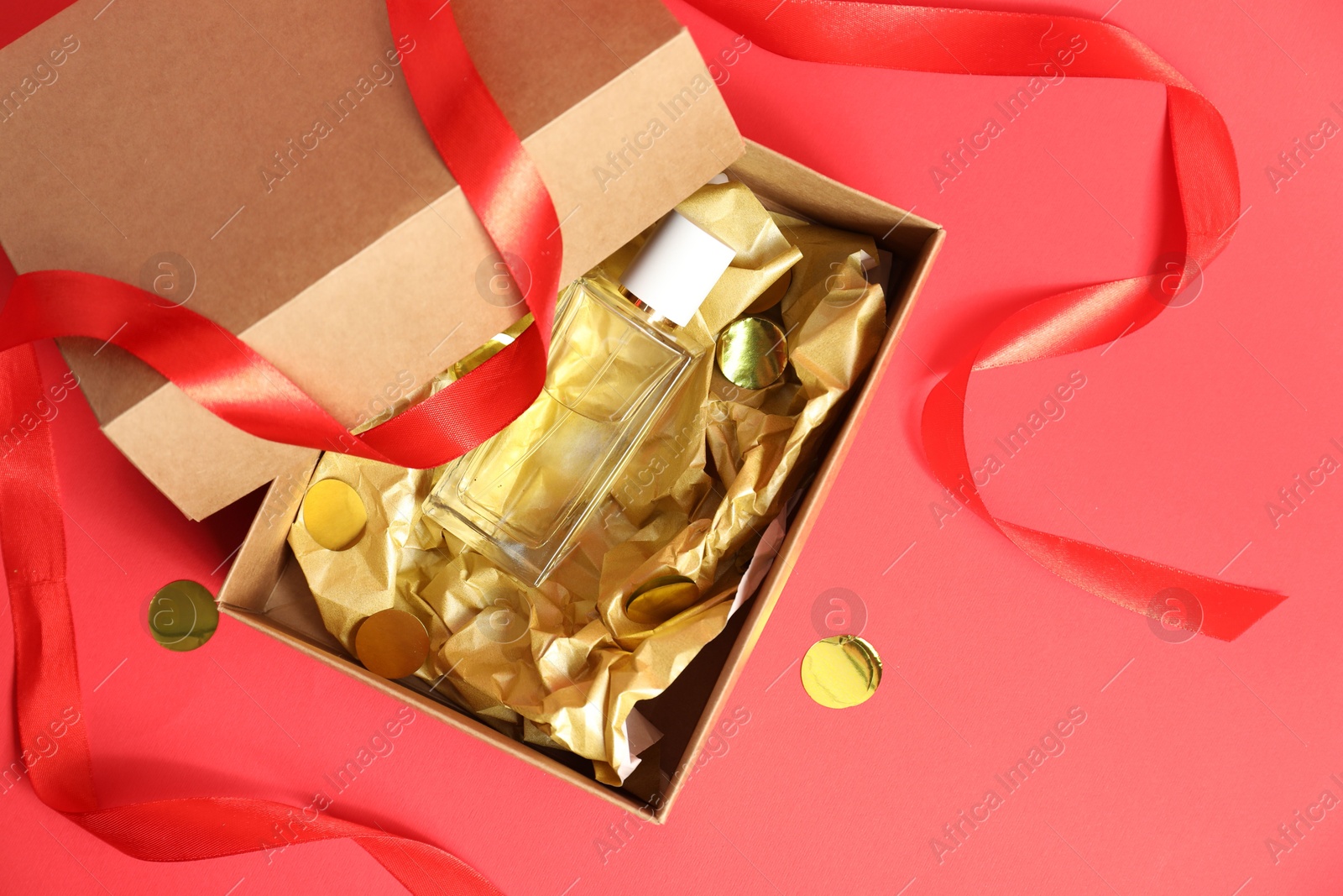 Photo of Open gift box with perfume bottle and confetti on red background, top view. Christmas present