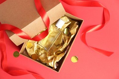 Open gift box with perfume bottle and confetti on red background, top view. Christmas present