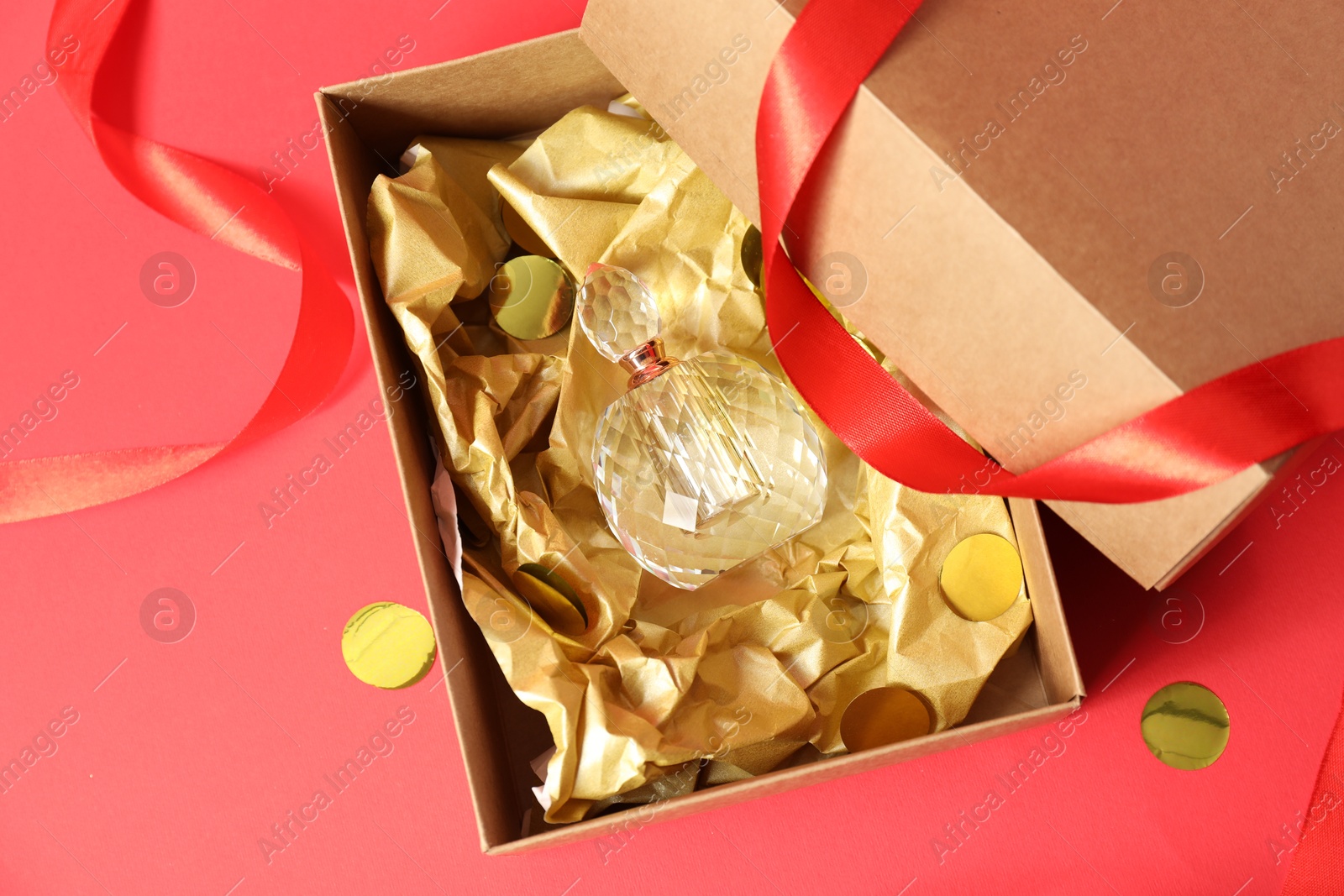 Photo of Open gift box with perfume bottle and confetti on red background, top view. Christmas present