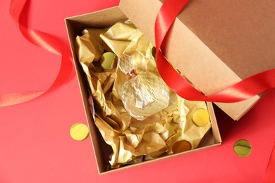 Open gift box with perfume bottle and confetti on red background, top view. Christmas present