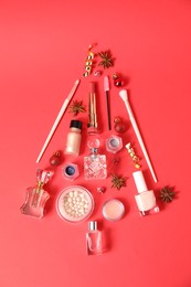 Photo of Christmas tree made of perfume bottles and makeup products on red background, flat lay