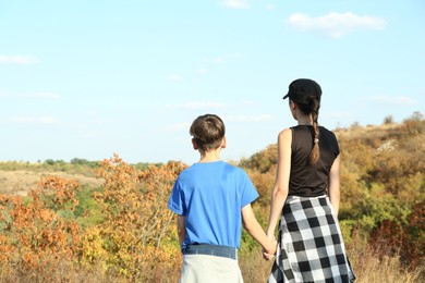 Photo of Mother and her son enjoying picturesque landscape on sunny day, back view. Space for text