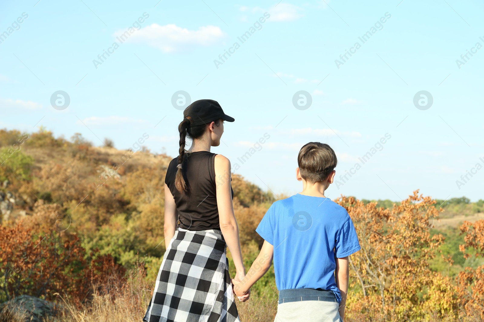 Photo of Mother and her son enjoying picturesque landscape on sunny day, back view