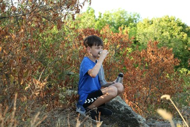 Photo of Little boy drinking tea among trees outdoors