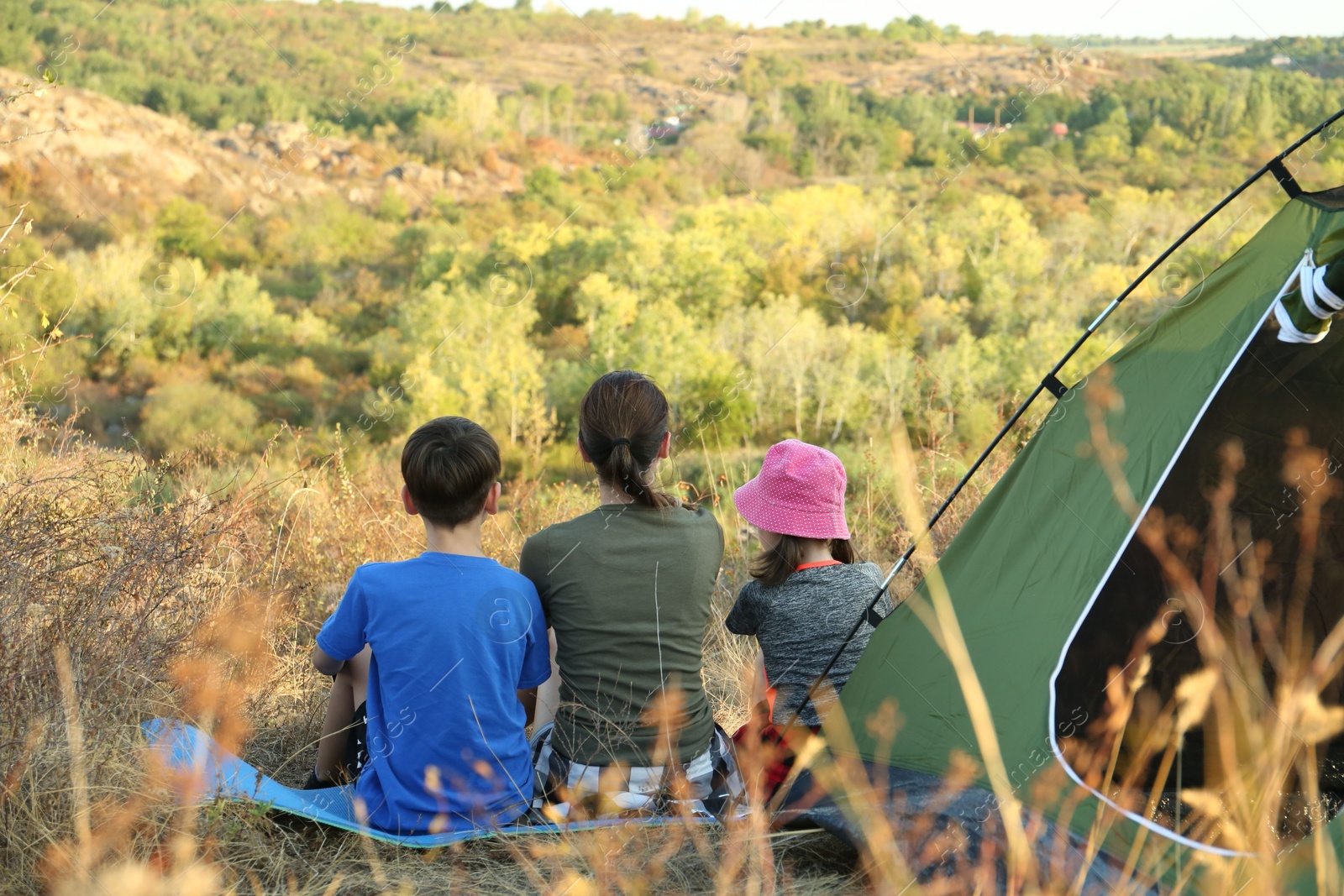 Photo of Family enjoying picturesque view near camping tent, back view