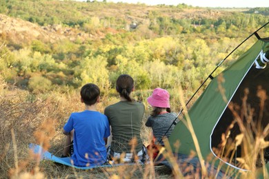 Photo of Family enjoying picturesque view near camping tent, back view