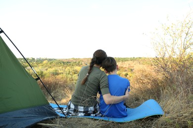 Photo of Mother and son enjoying picturesque view near camping tent, back view