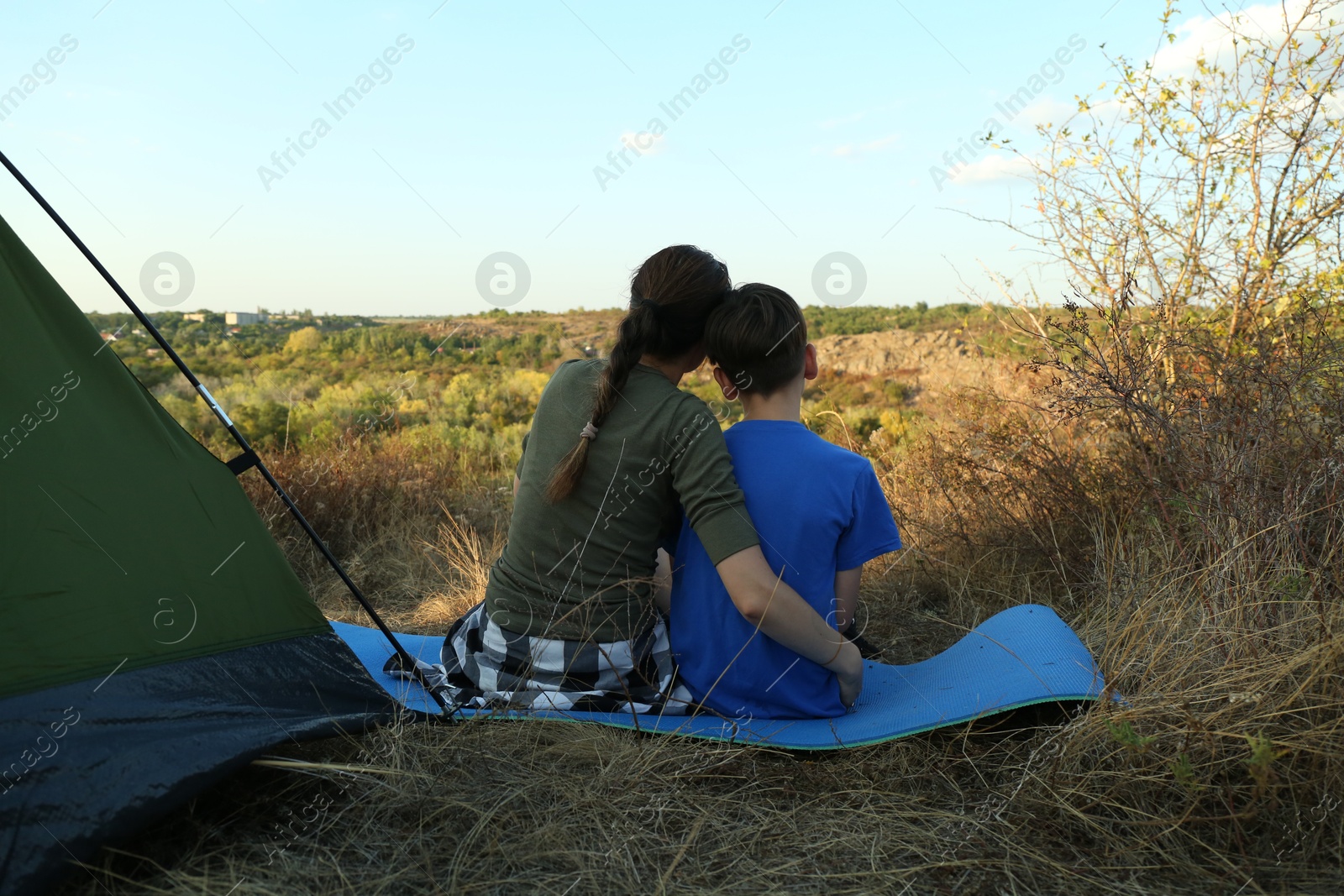 Photo of Mother and son enjoying picturesque view near camping tent, back view