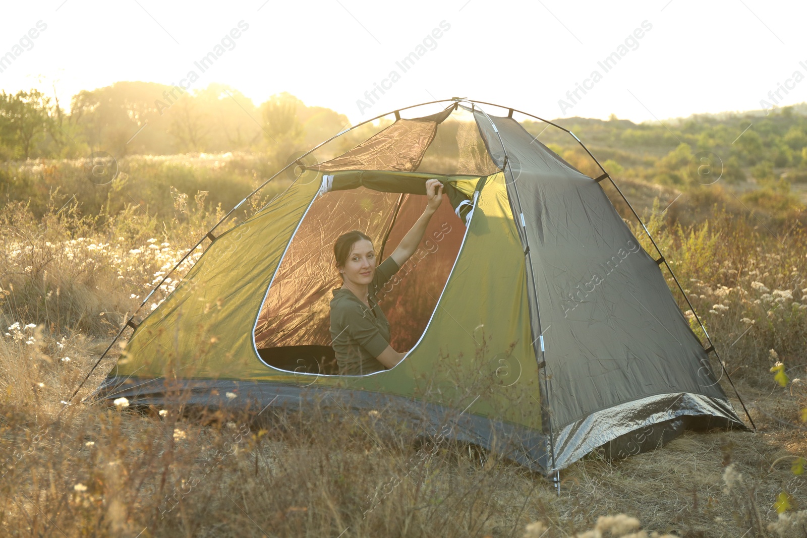 Photo of Woman in camping tent among plants outdoors on sunny day