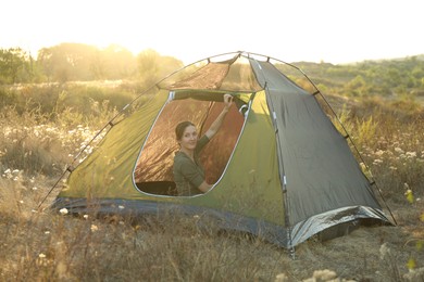 Woman in camping tent among plants outdoors on sunny day