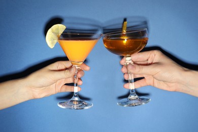 Photo of Friends with glasses of refreshing cocktails on blue background, closeup