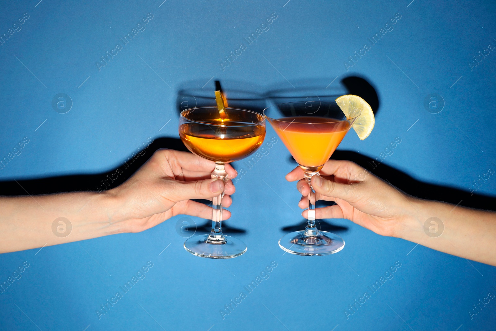 Photo of Friends with glasses of refreshing cocktails on blue background, closeup