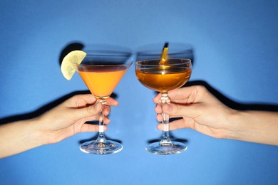 Photo of Friends with glasses of refreshing cocktails on blue background, closeup