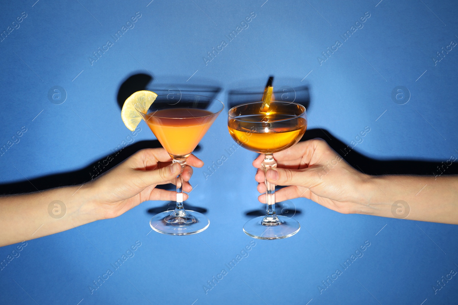 Photo of Friends with glasses of refreshing cocktails on blue background, closeup