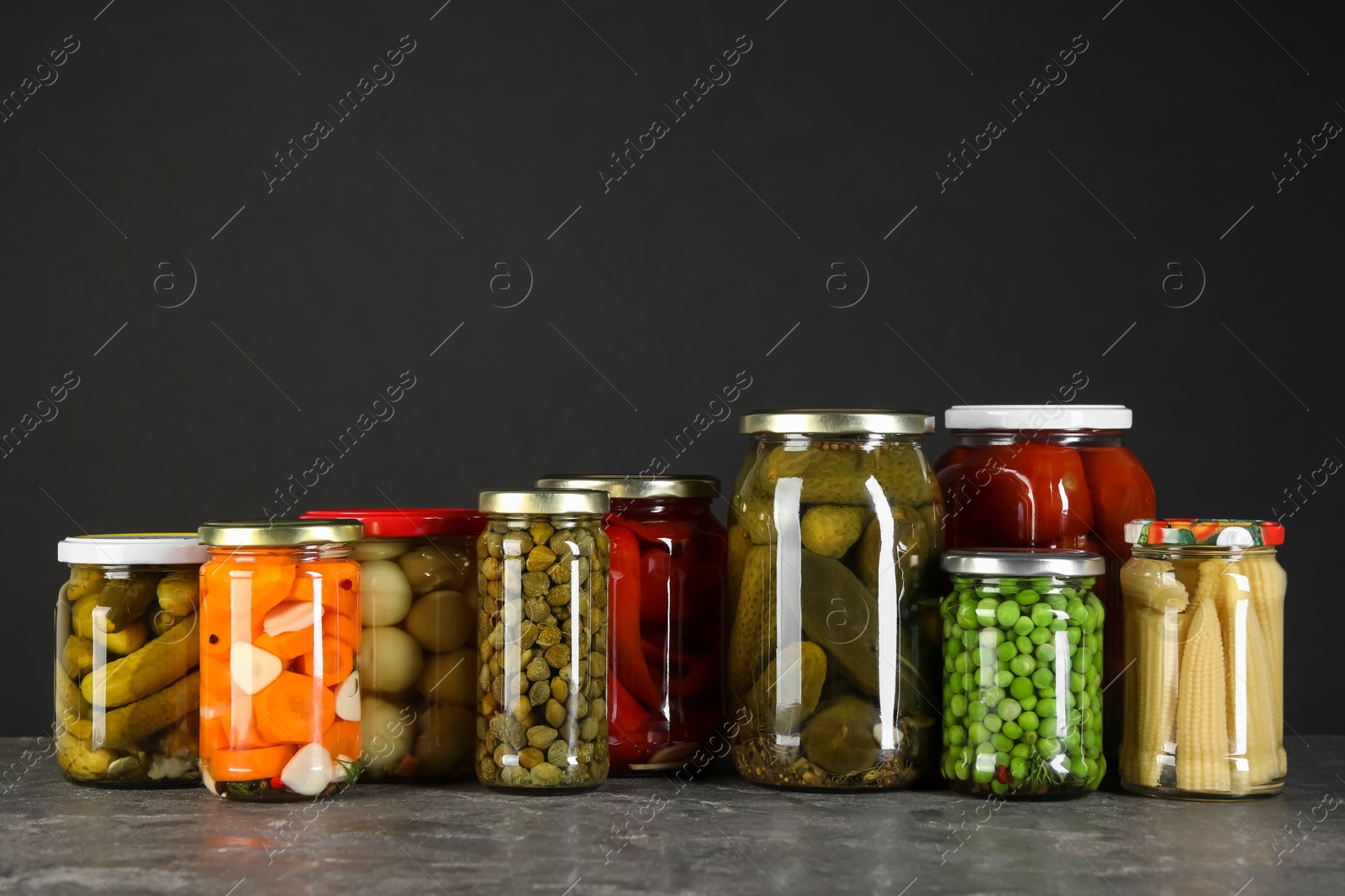 Photo of Different pickled products in jars on grey textured table