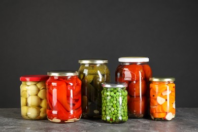 Photo of Different pickled products in jars on grey textured table