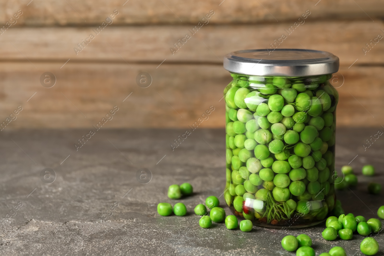 Photo of Tasty pickled green peas in jar on grey textured table, space for text