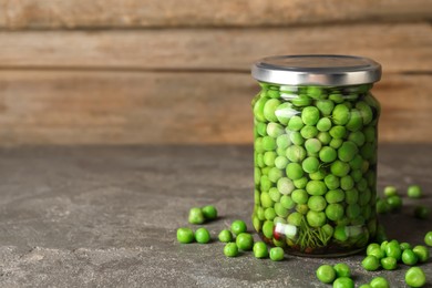 Photo of Tasty pickled green peas in jar on grey textured table, space for text