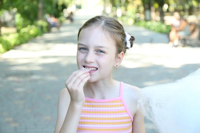 Portrait of little girl eating sweet cotton candy in park