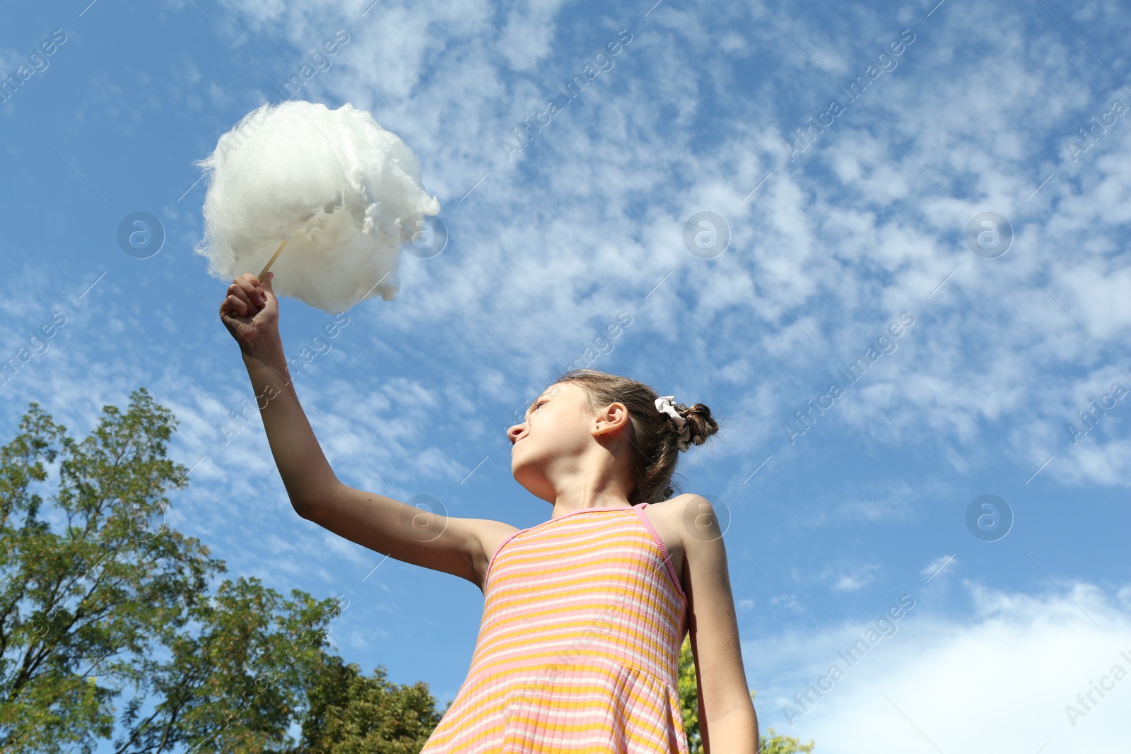 Photo of Little girl with sweet cotton candy against blue sky in park, low angle view