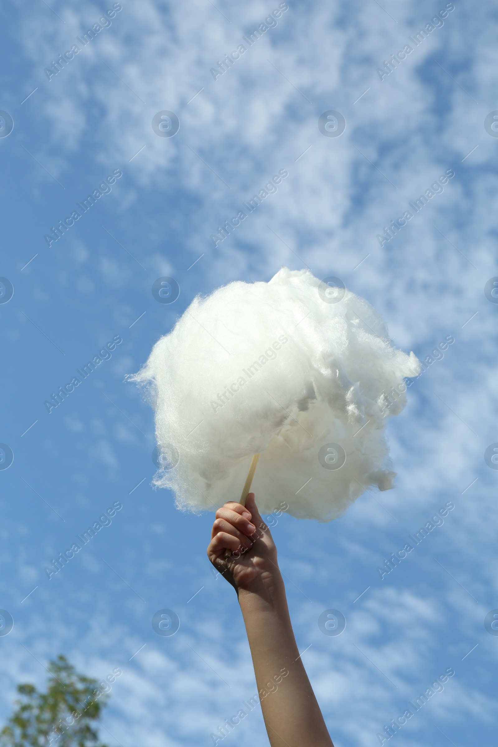 Photo of Little girl holding sweet cotton candy against blue sky in park, closeup