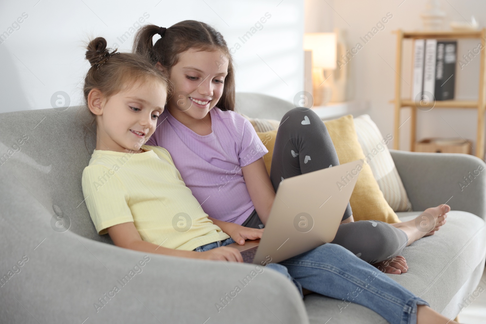 Photo of Cute little sisters with laptop spending time together at home