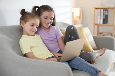 Cute little sisters with laptop spending time together at home