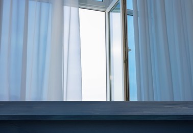 Image of Empty blue wooden table near window with curtains. Space for design